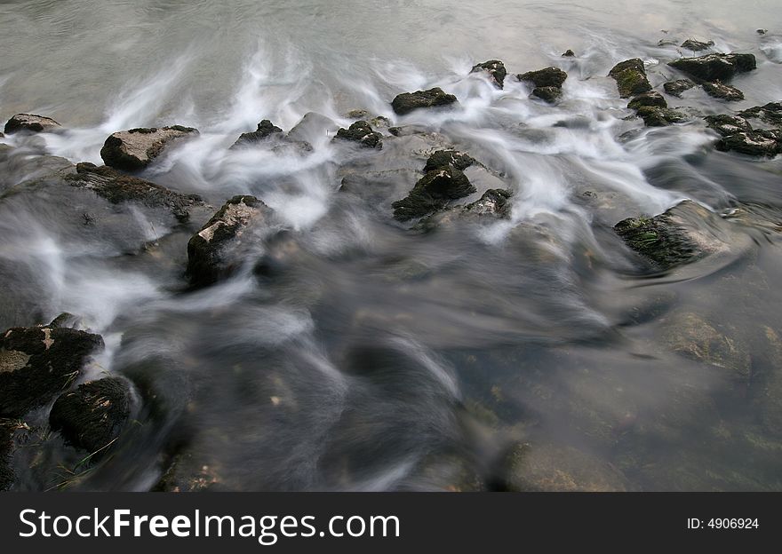 Long exposure shot of the river flowing cross the stones covered with moss. River Kolpa. Dolenjska. Slovenia