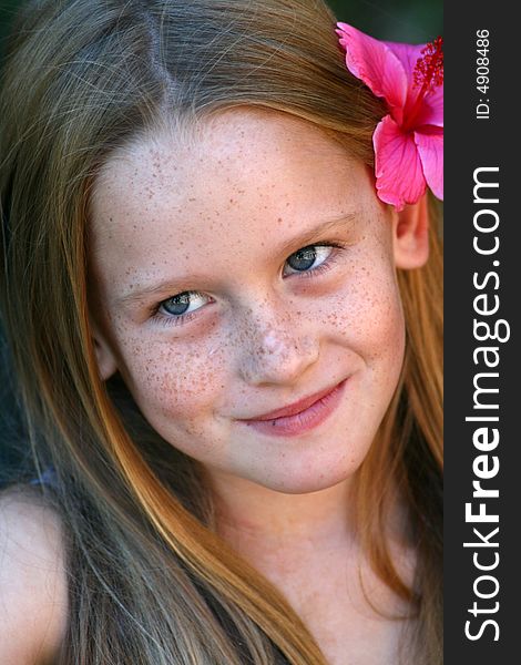 A white caucasian girl child with a pink flower in her hair smiling softly. A white caucasian girl child with a pink flower in her hair smiling softly