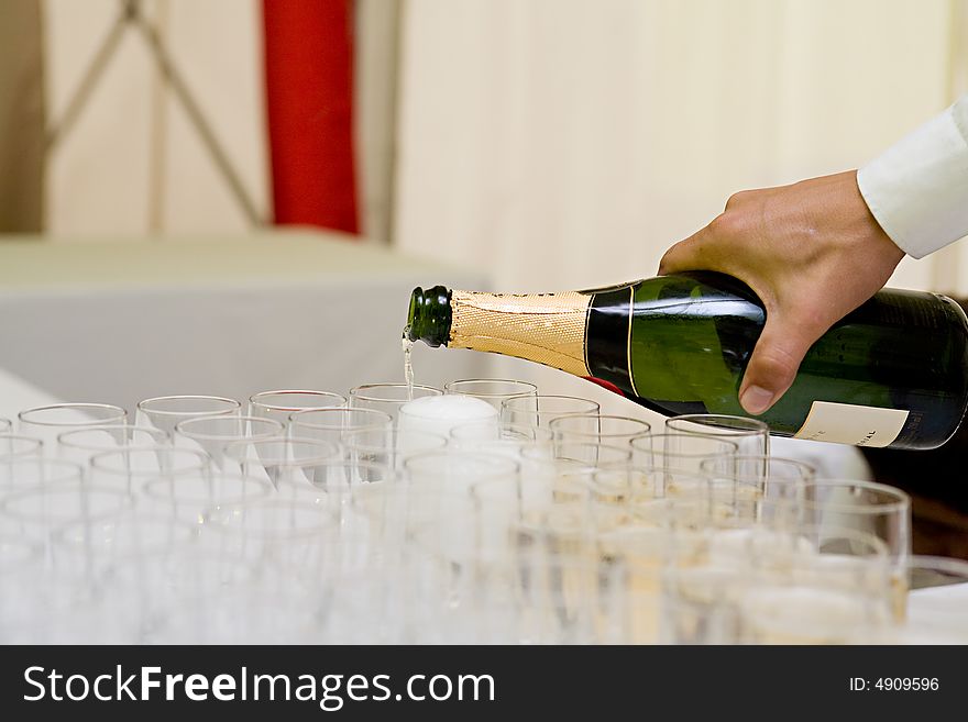 The hand of the waiter holds a bottle of champagne which it spills in the glasses standing on a table. The hand of the waiter holds a bottle of champagne which it spills in the glasses standing on a table