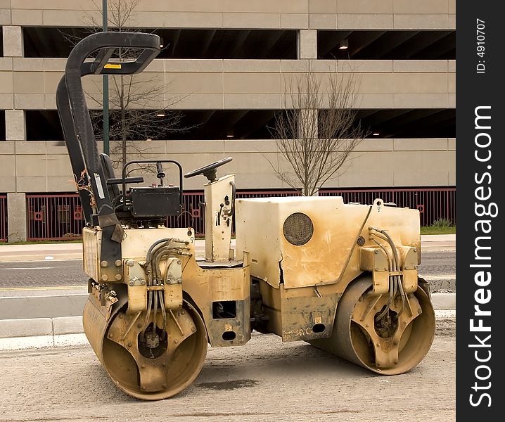 An old dirty paving roller on a new road in front of a parking deck. An old dirty paving roller on a new road in front of a parking deck