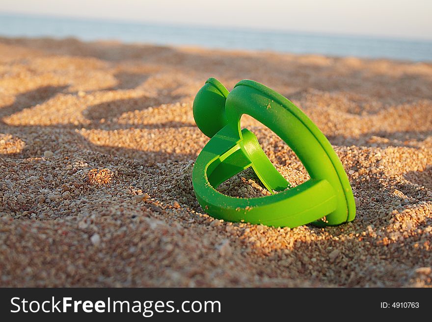 Part of toy is laying on sand during sunset. Part of toy is laying on sand during sunset