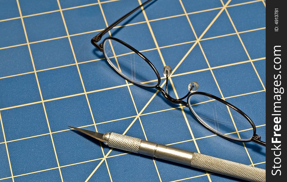 Razor knife and reading glasses on a blue cutting mat. Razor knife and reading glasses on a blue cutting mat
