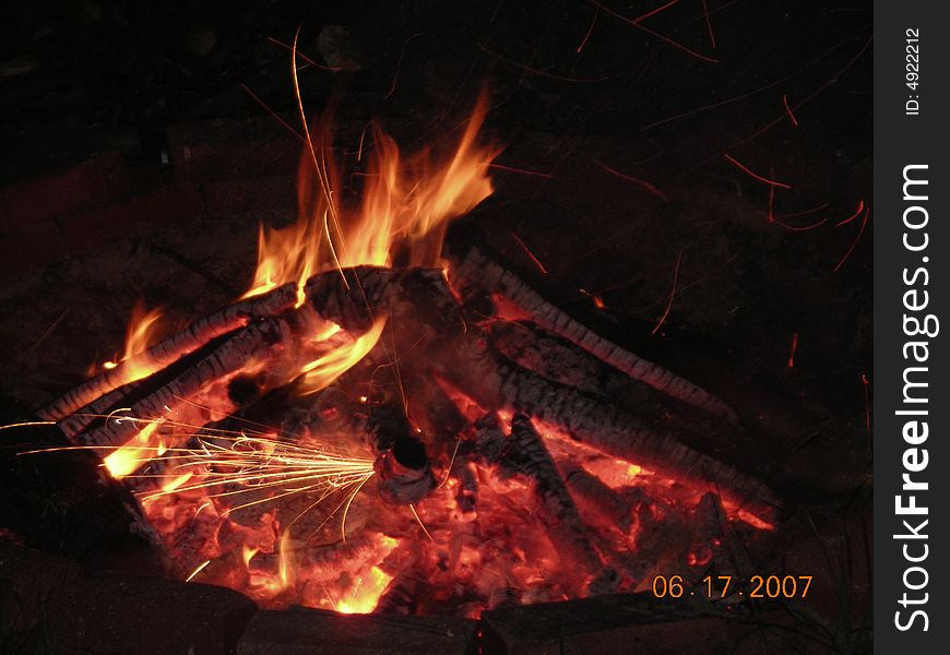 Picture of a blazing fire with fire crackers thrown into the fire causing the ambers to fly up and glow. Picture of a blazing fire with fire crackers thrown into the fire causing the ambers to fly up and glow.