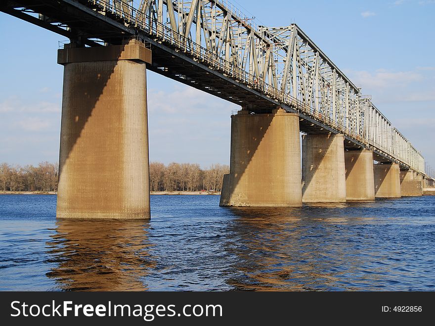 Train bridge over wide river in sunny day with supports mirroring in wavy water. Train bridge over wide river in sunny day with supports mirroring in wavy water