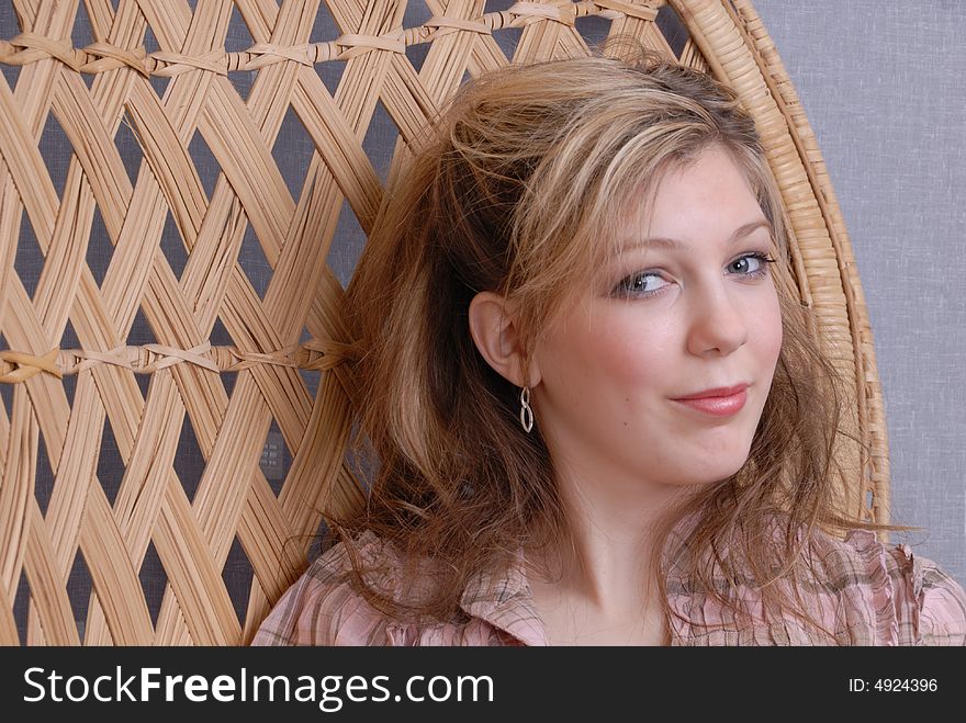 Thoughtful pretty young blonde teenage girl on wickerwork seat holding straw hat. Thoughtful pretty young blonde teenage girl on wickerwork seat holding straw hat