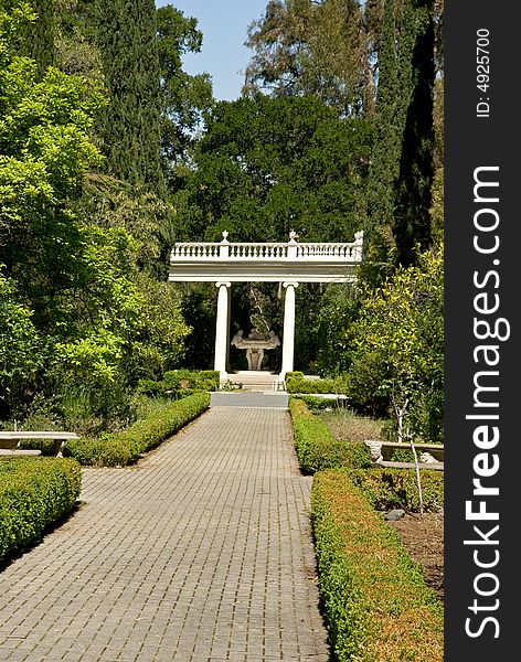 Empty footpath perspective in blooming garden with classic pavilion