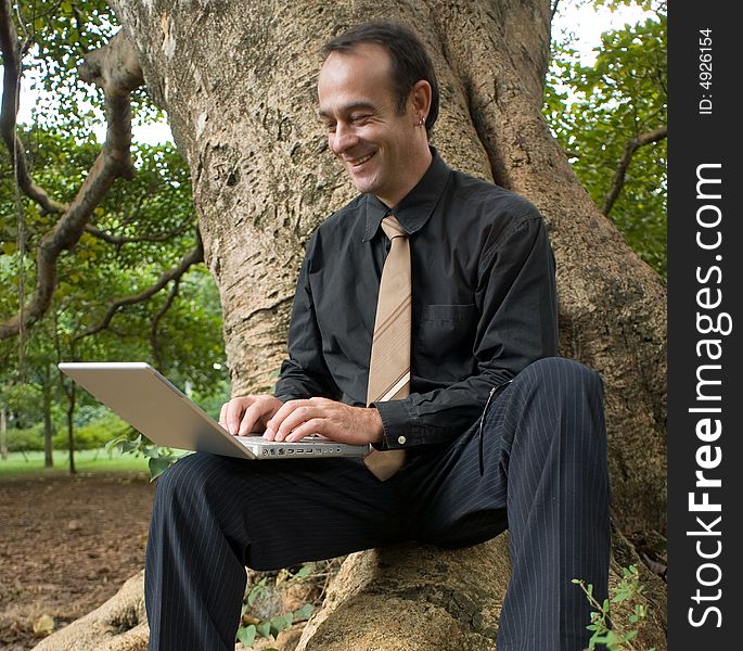 A businessman sitting on giant tree's roots using a laptop. A businessman sitting on giant tree's roots using a laptop.