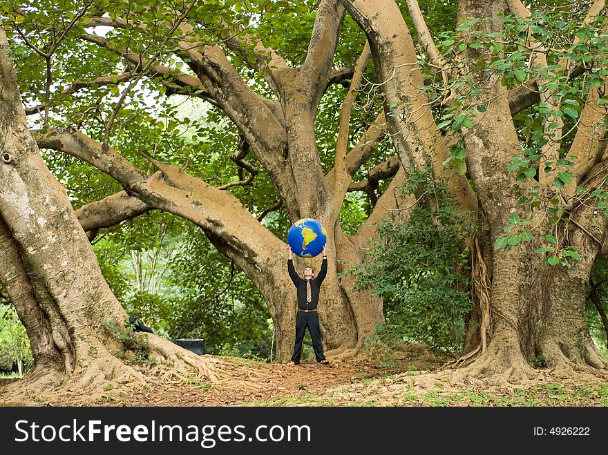 Wide angle shot of a Latin American businessman standing in a grove of trees with an inflatable globe held above his head. Wide angle shot of a Latin American businessman standing in a grove of trees with an inflatable globe held above his head