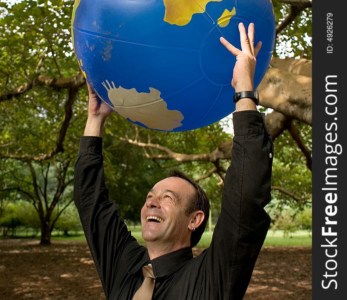 Latin American businessman standing in a grove of trees with an inflatable globe held above his head. Latin American businessman standing in a grove of trees with an inflatable globe held above his head