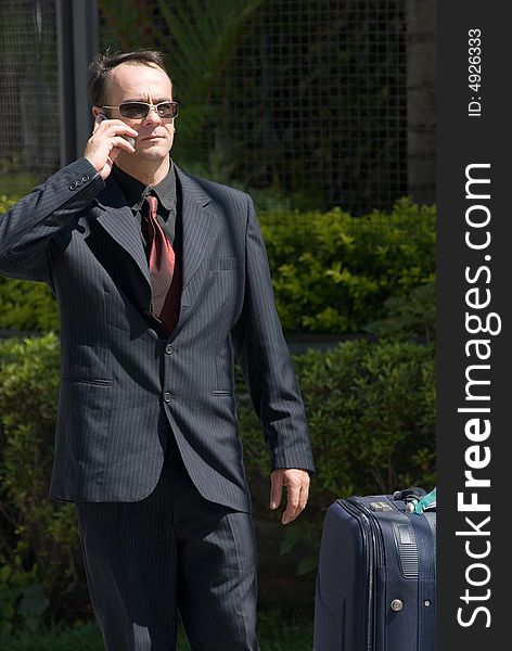 Latin american businessman standing by his luggage and talking on his cell phone. Latin american businessman standing by his luggage and talking on his cell phone