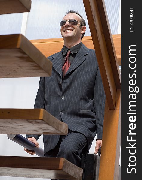 Latin american businessman smiling while walking up the stairs holding a briefcase and a set of rolled up plans. Latin american businessman smiling while walking up the stairs holding a briefcase and a set of rolled up plans