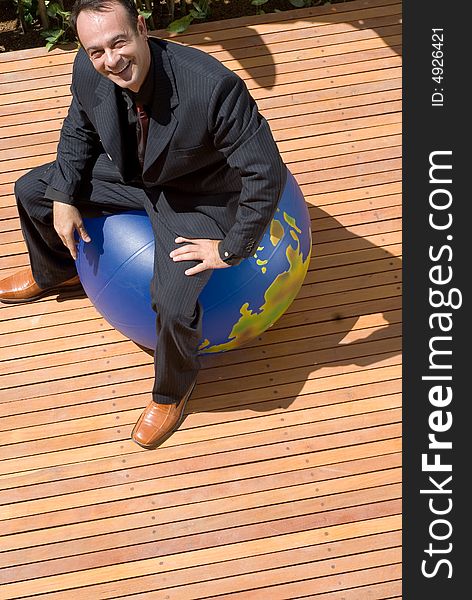 Latin american businessman sitting on top of an inflatable globe with a large smile on his face. Latin american businessman sitting on top of an inflatable globe with a large smile on his face