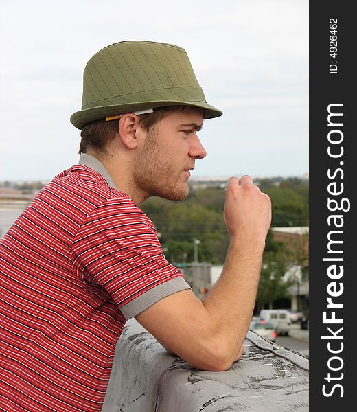 A man on a roof top wearing a green hat with a cigarette behind his ear. A man on a roof top wearing a green hat with a cigarette behind his ear.
