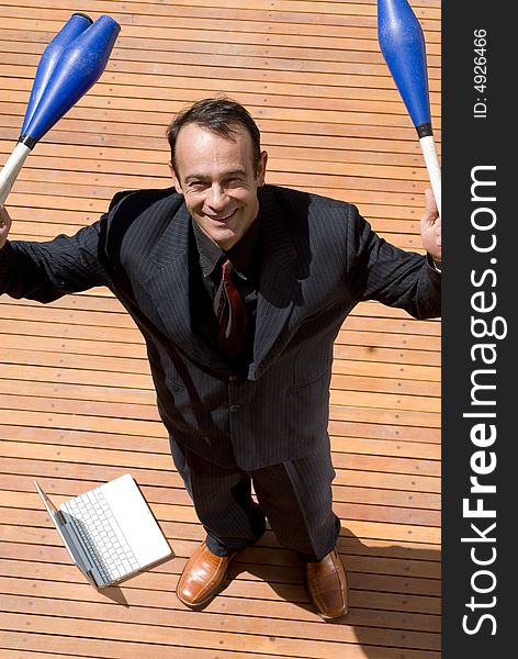 A businessman standing, with a laptop at his feet, holding juggling pins. A businessman standing, with a laptop at his feet, holding juggling pins.