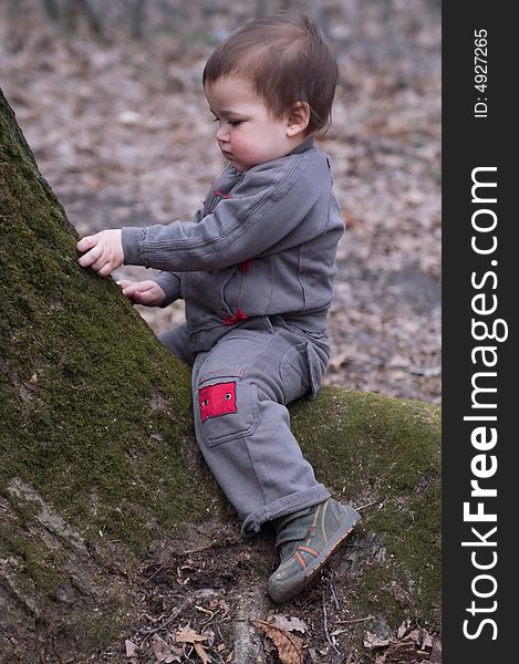 Thoughtful child in brown dress sitting on green moss tree at autumn day