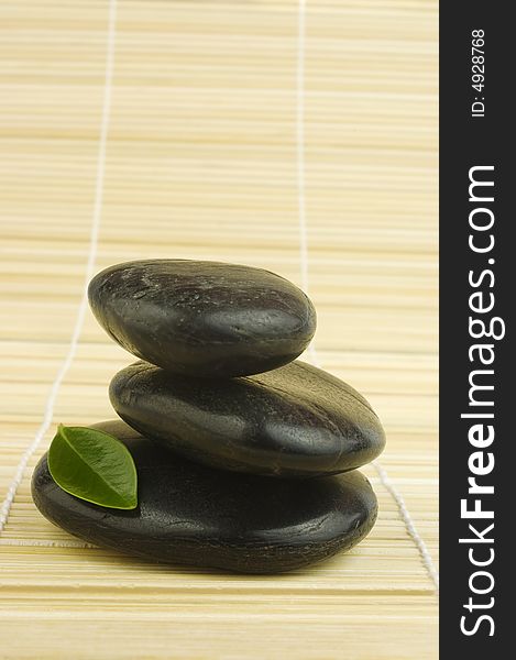 Black zen pebbles and green leaf on bamboo