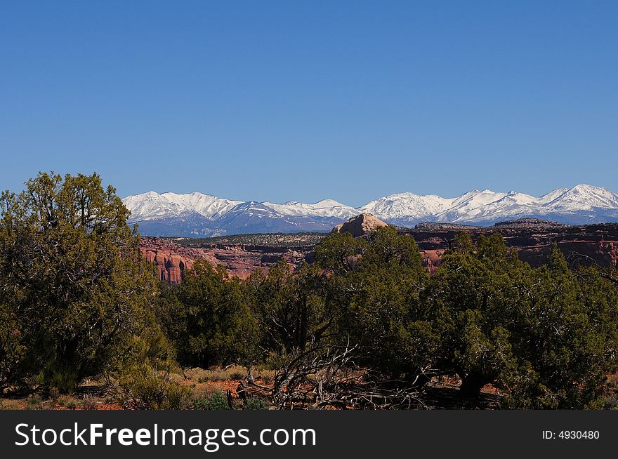 Beautiful vista of snow capped mountains, red rock canyon and green trees against blue sky. Beautiful vista of snow capped mountains, red rock canyon and green trees against blue sky.