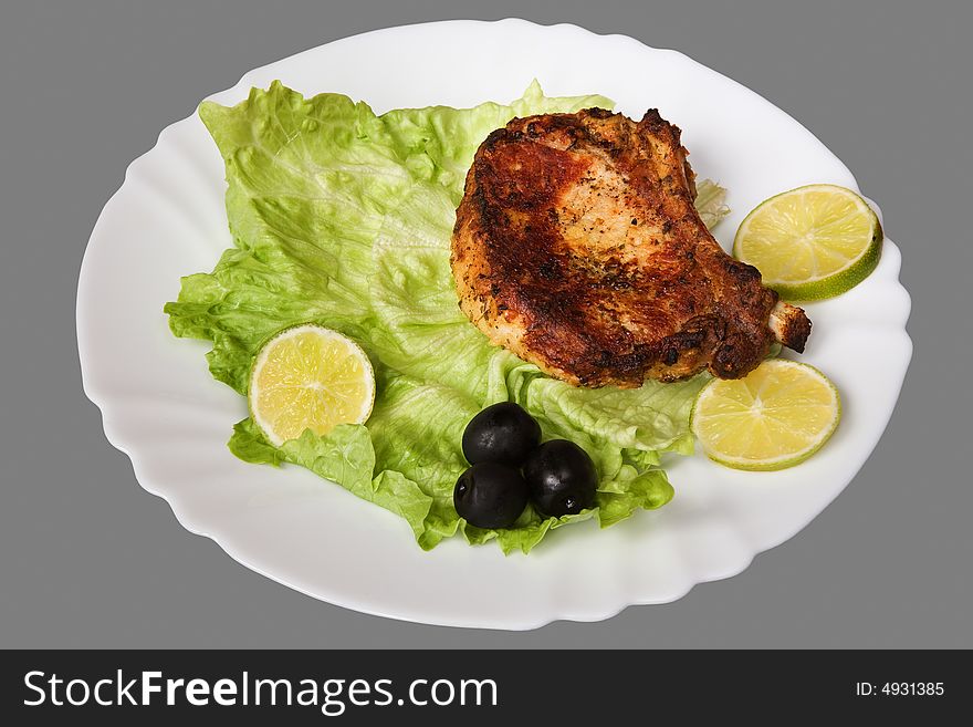 Piece appetizing grilled meat on a plate with a leaf of salad, lemons and olives. Isolated on grey [with clipping path]. Piece appetizing grilled meat on a plate with a leaf of salad, lemons and olives. Isolated on grey [with clipping path].