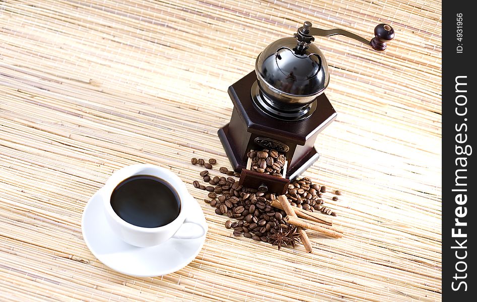 Cup of coffee, grinder, coffee beans and sticks of cinnamon.