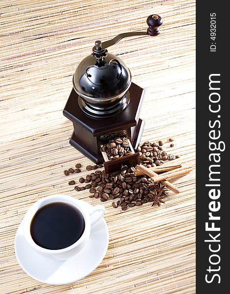 Coffee grinder, cup of coffee, coffee beans and sticks of cinnamon.