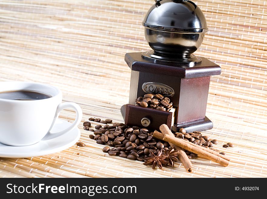 Grinder, cup of coffee, coffee beans and sticks of cinnamon.