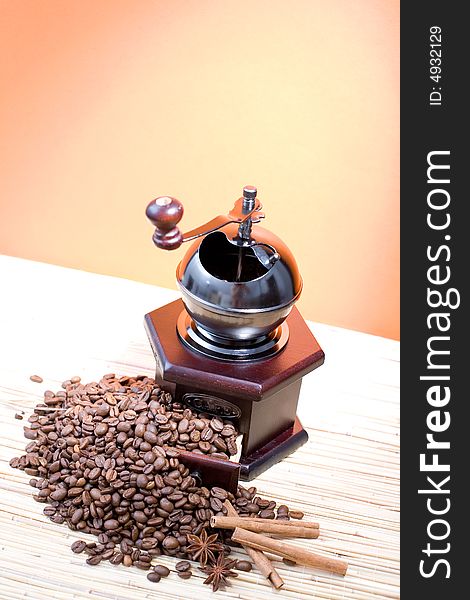 Grinder, coffee beans and sticks of cinnamon on hot orange background.