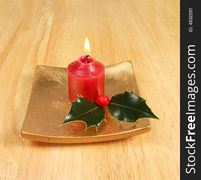 Burning candle with holly on a gold platter as a Christmas theme