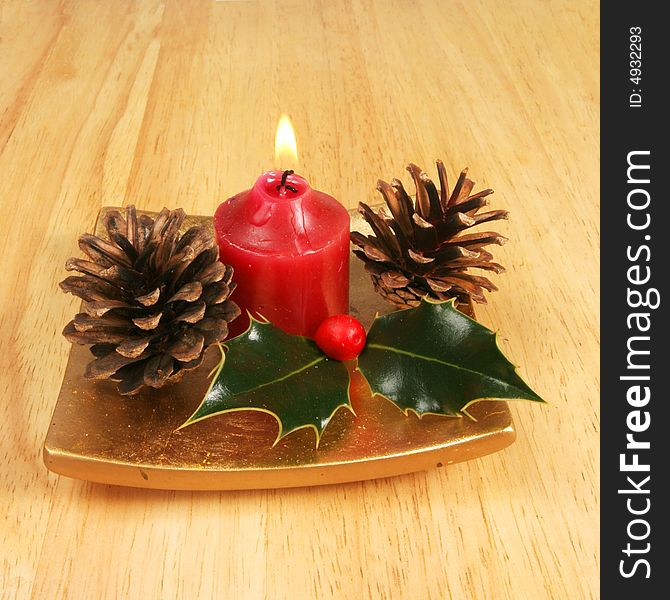 Candle with holly and pine cones on a gold platter as a Christmas theme. Candle with holly and pine cones on a gold platter as a Christmas theme