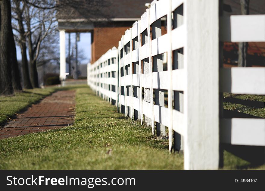 Brick sidewalk lined with a white wooden fence. Brick sidewalk lined with a white wooden fence.