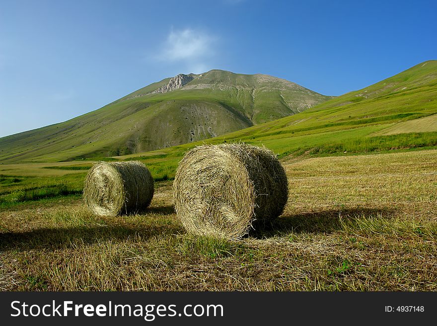 Enormous Hay Balls at the feet of a Mountain. This is a very High Plateau. It's a Summertime afternoon (June) . Enormous Hay Balls at the feet of a Mountain. This is a very High Plateau. It's a Summertime afternoon (June) .