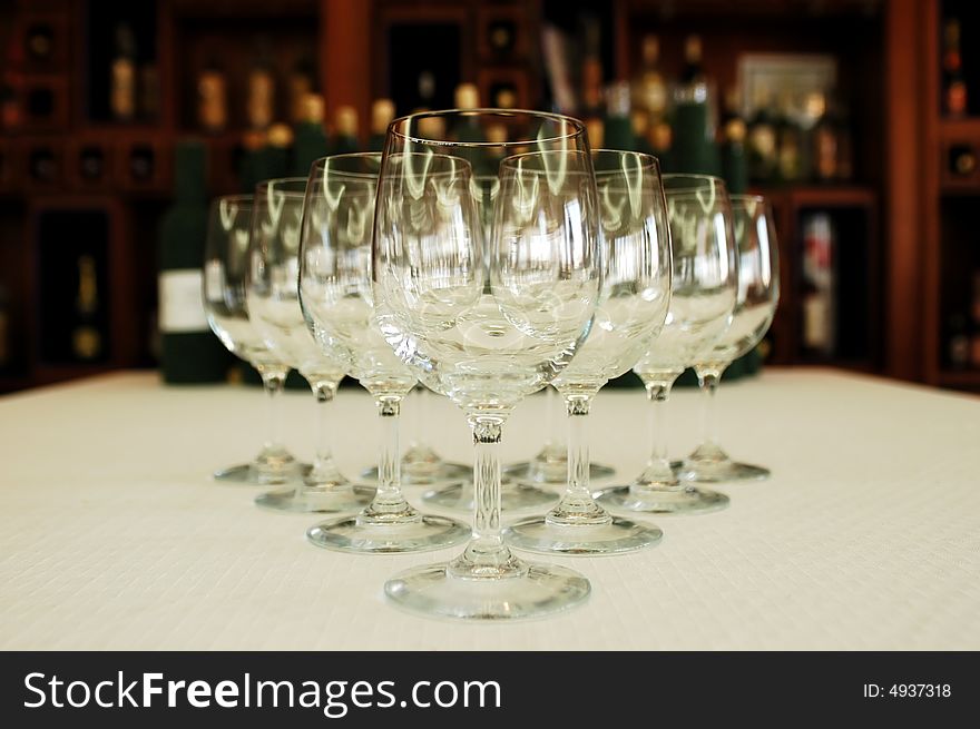 Wine glasses in a row, wine bottles on background, focus on glass. Wine glasses in a row, wine bottles on background, focus on glass