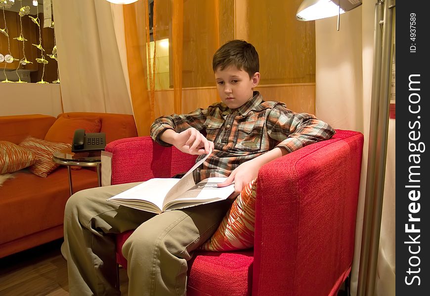 The boy sitting in a red armchair and reading the book. The boy sitting in a red armchair and reading the book