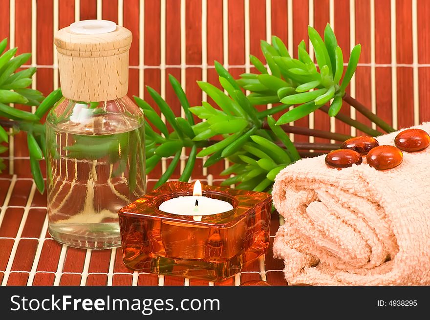 Aromatherapy bottle, glass pebbles, towel, candle and green plants on bamboo. Aromatherapy bottle, glass pebbles, towel, candle and green plants on bamboo