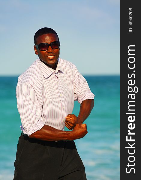 Businessman flexing on the beach with blue water in the background. Businessman flexing on the beach with blue water in the background.