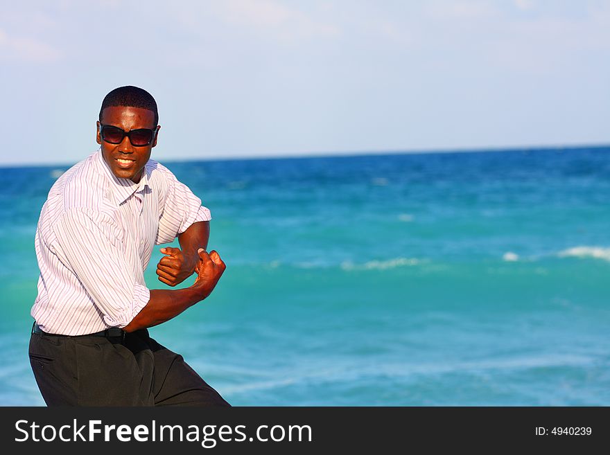 Businessman flexing on the beach with blue water in the background. Businessman flexing on the beach with blue water in the background.