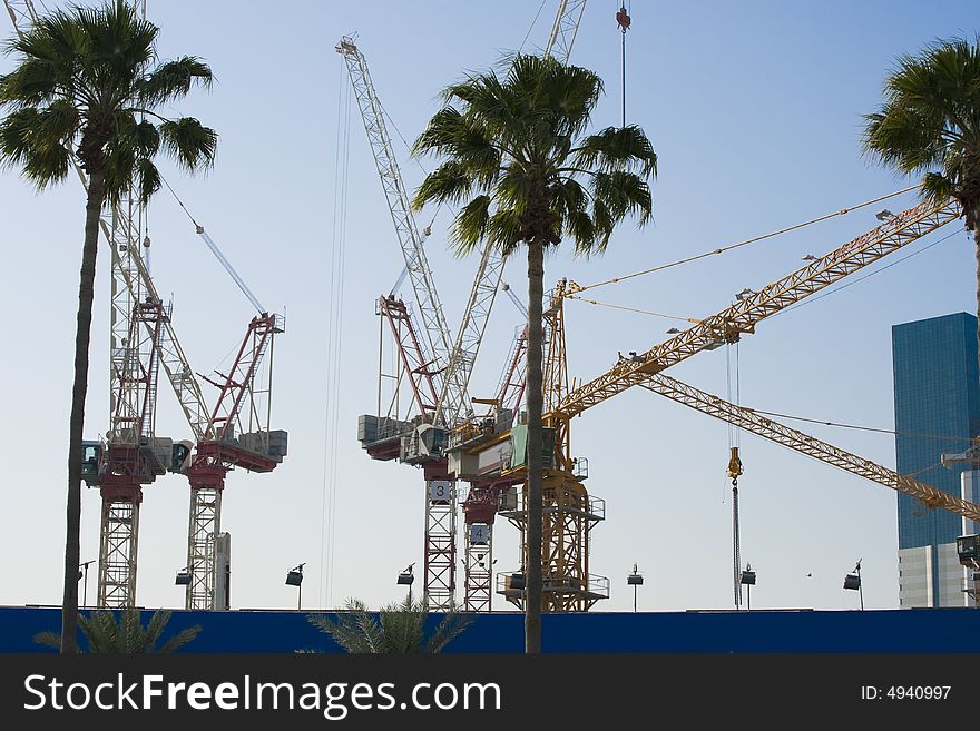 Cranes towering into the sky aiding the construction of new skyscrapers. There are palm trees in the foreground etched against the late afternoon skies. Cranes towering into the sky aiding the construction of new skyscrapers. There are palm trees in the foreground etched against the late afternoon skies.