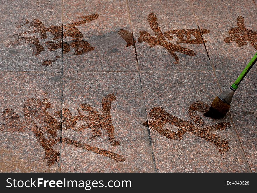 A man writing Chinese characters with a big brush on the ground. A man writing Chinese characters with a big brush on the ground.