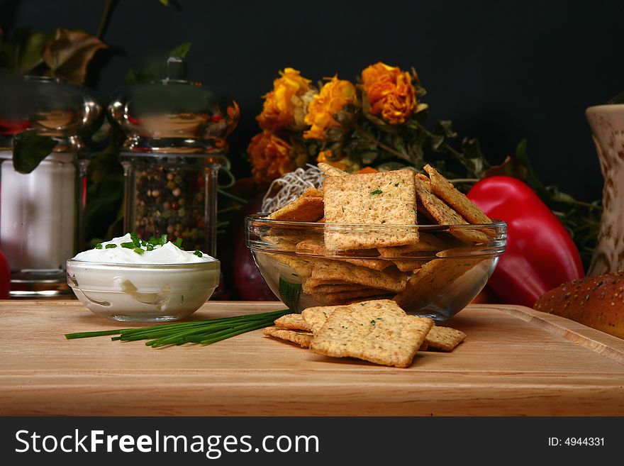 Square sour cream and chive flavored crackers in glass bowl on cutting board in kitchen or resturant.