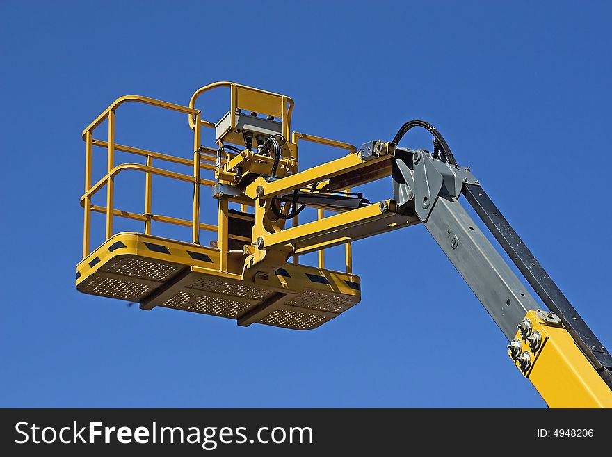 Yellow construction crane basket against blue sky.