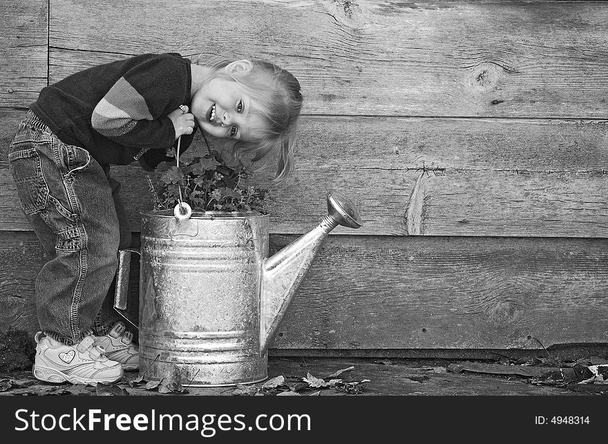 Little girl with watering can by an old barn. Little girl with watering can by an old barn.