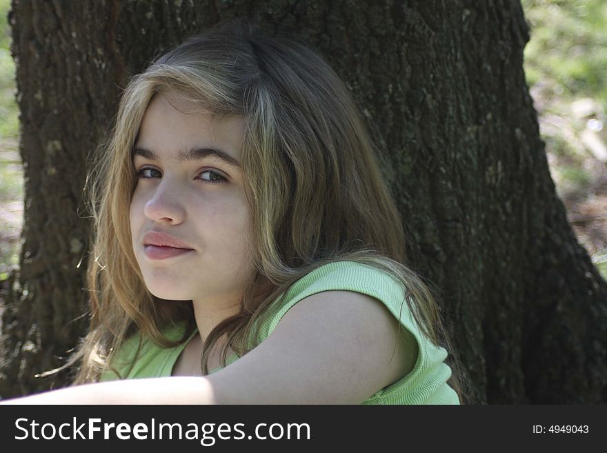 Young girl sitting on ground against tree. Young girl sitting on ground against tree