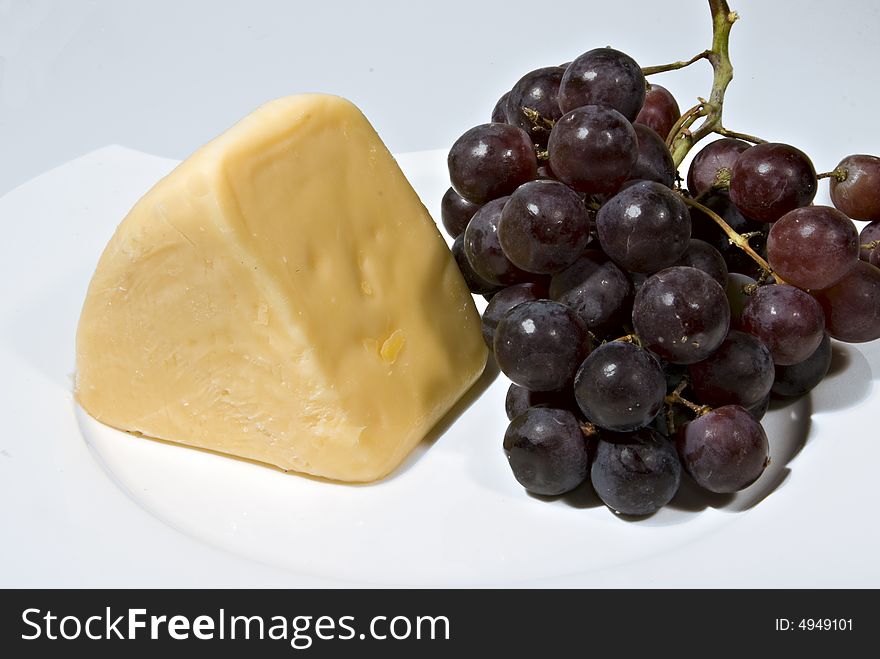 A wedge of cheese and bunch of red seedless grapes. A wedge of cheese and bunch of red seedless grapes.