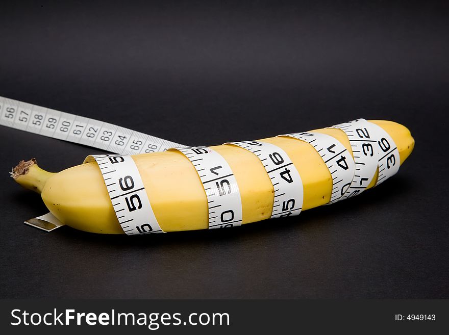 A banana with a tape measure wrapped around it in a spiral isolated on a black background. A banana with a tape measure wrapped around it in a spiral isolated on a black background.