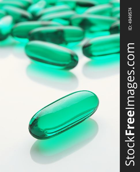 Green capsules on white background, vertical image