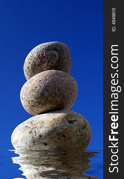 Stack of pebbles and reflection in water with blue sky background