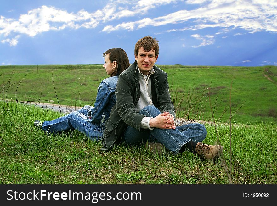 Guy and girl sits on a grass on a background of the sky