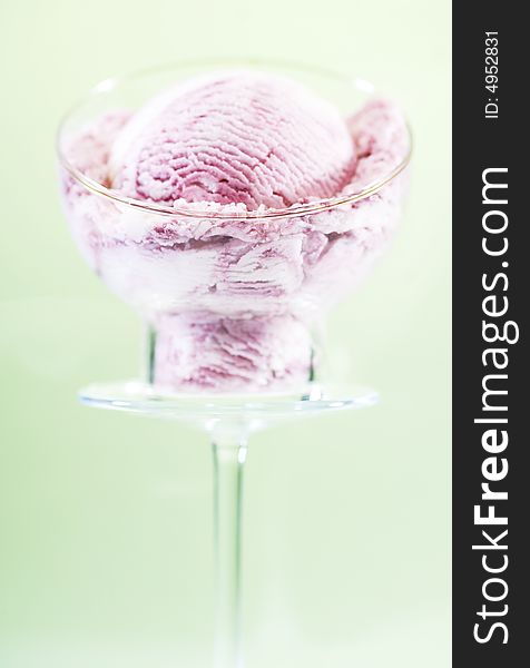 A scoop of raspberry ice cream in a glass cup on a pedestal. Green background. A scoop of raspberry ice cream in a glass cup on a pedestal. Green background