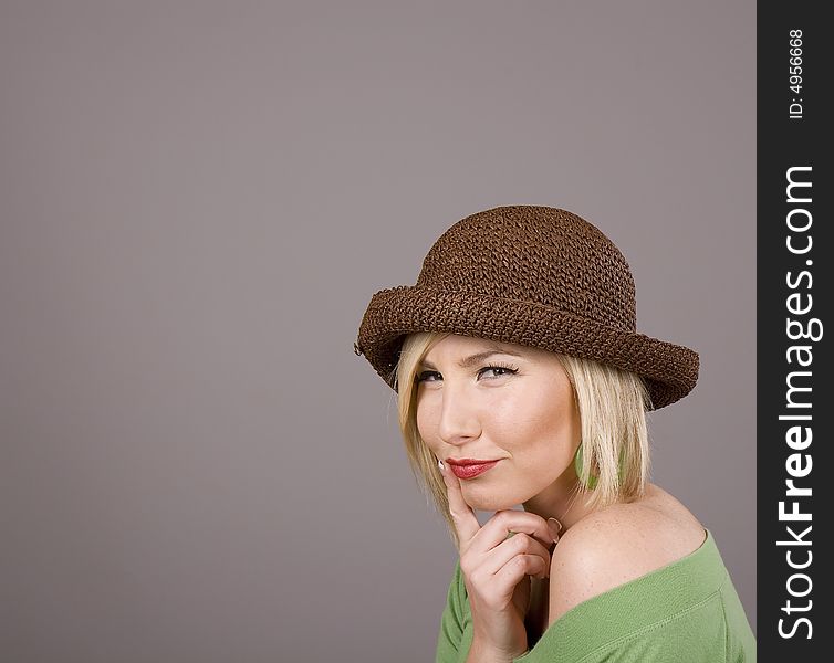 A blonde in a green blouse and silly brown hat with her finger on her lips. A blonde in a green blouse and silly brown hat with her finger on her lips