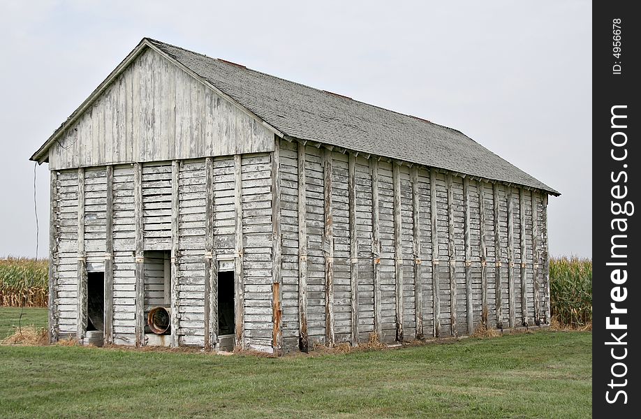 An old corn crib with a corn field behind it.