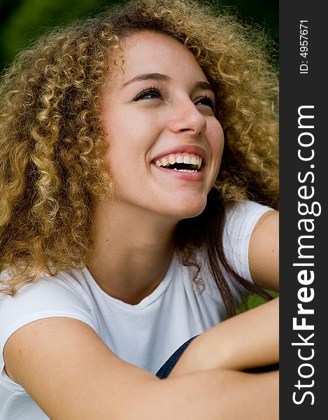 A young attractive woman sitting outside in the park laughing. A young attractive woman sitting outside in the park laughing